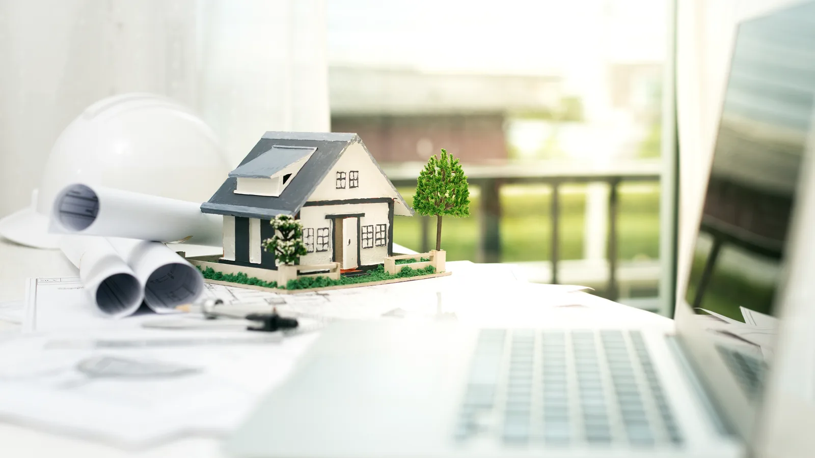 Maqueta de una vivienda junto a planos arquitectónicos y un ordenador